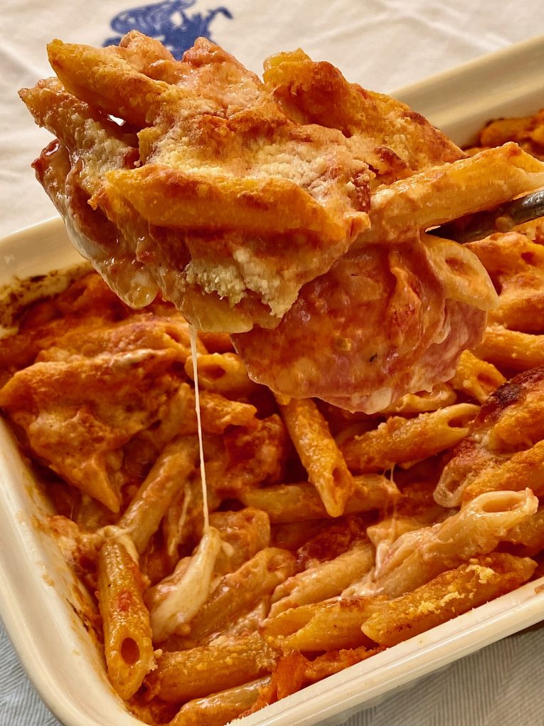Fork lifting cheesy baked penne pasta from a casserole dish, with melted mozzarella and a golden, crispy topping